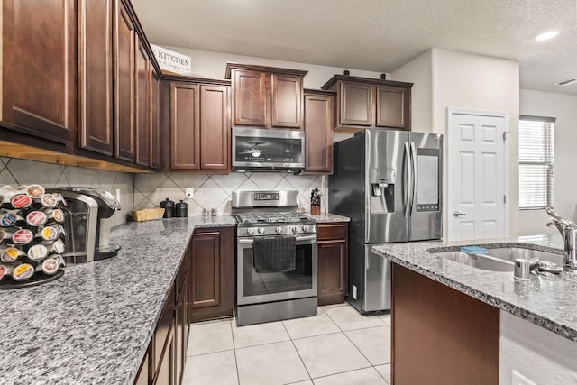 kitchen featuring appliances with stainless steel finishes, tasteful backsplash, light stone counters, sink, and light tile floors