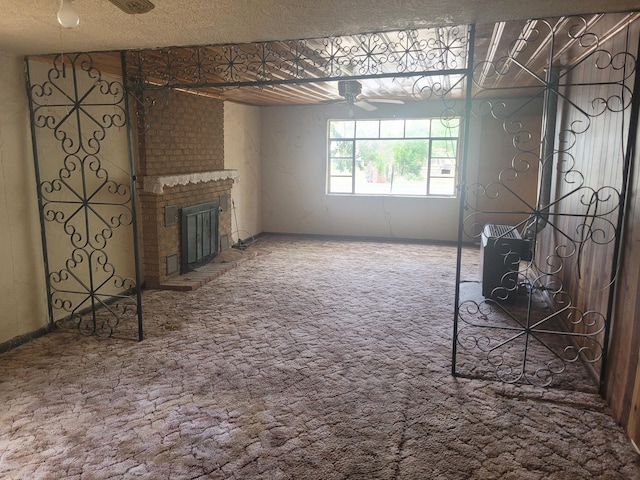 unfurnished living room featuring a textured ceiling, brick wall, a brick fireplace, carpet flooring, and ceiling fan