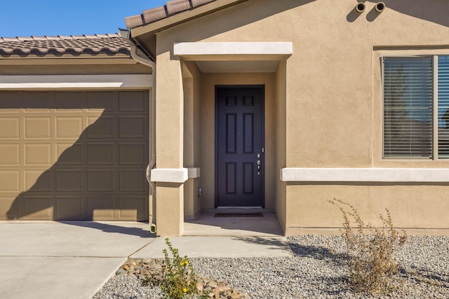 property entrance featuring a tiled roof, an attached garage, driveway, and stucco siding