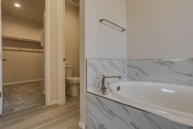 full bathroom featuring a garden tub, toilet, wood finish floors, baseboards, and a spacious closet