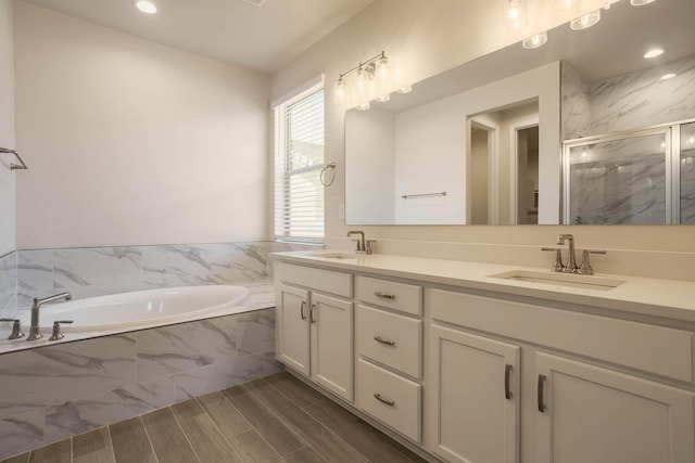 bathroom with a garden tub, a sink, a marble finish shower, and double vanity