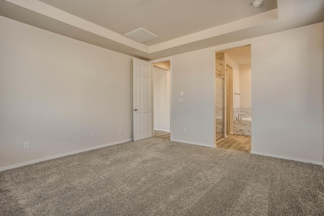 spare room with carpet floors, a raised ceiling, visible vents, and baseboards