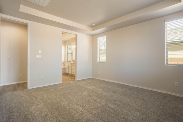 unfurnished bedroom featuring a raised ceiling, light carpet, baseboards, and ensuite bathroom