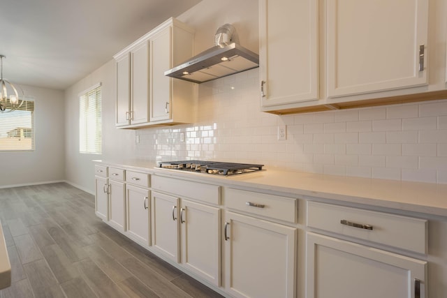 kitchen featuring stainless steel gas cooktop, dark wood-type flooring, light countertops, range hood, and tasteful backsplash