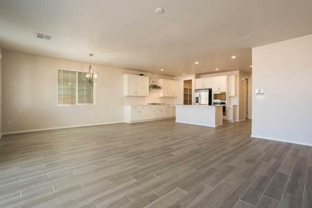 unfurnished living room with a notable chandelier, recessed lighting, visible vents, light wood-type flooring, and baseboards