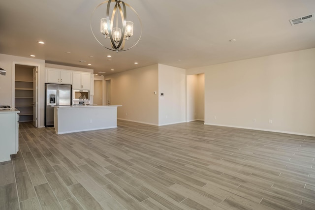 unfurnished living room featuring recessed lighting, visible vents, an inviting chandelier, light wood-style floors, and baseboards