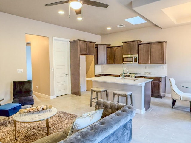 kitchen featuring tasteful backsplash, an island with sink, sink, a kitchen bar, and ceiling fan