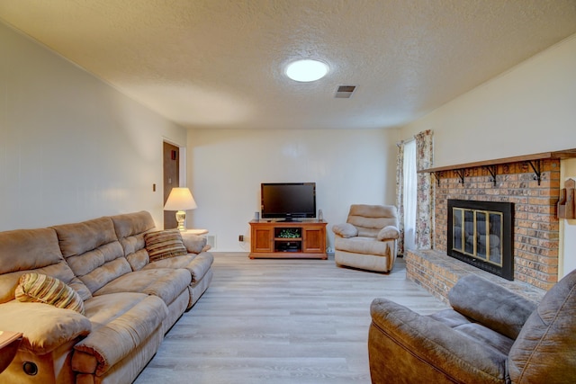 living room featuring a textured ceiling, a brick fireplace, and light wood-type flooring