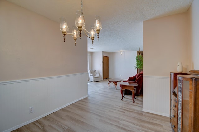 interior space with an inviting chandelier, a textured ceiling, and light wood-type flooring