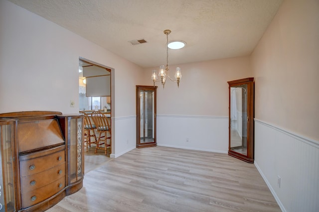 unfurnished dining area featuring an inviting chandelier, a textured ceiling, and light wood-type flooring