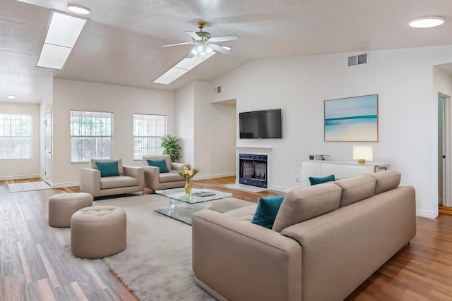 living room featuring ceiling fan, hardwood / wood-style floors, and vaulted ceiling with skylight