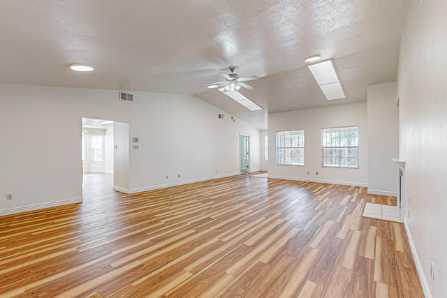 empty room with ceiling fan, light hardwood / wood-style flooring, a textured ceiling, and lofted ceiling with skylight