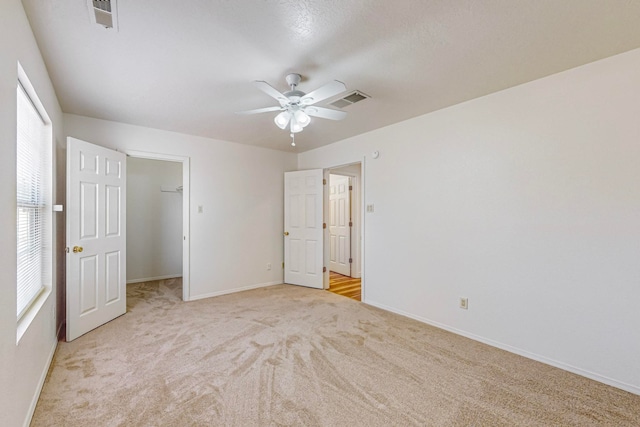 unfurnished bedroom with light carpet, a walk in closet, a closet, and ceiling fan