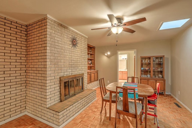 dining area featuring ceiling fan, light parquet flooring, brick wall, and a brick fireplace