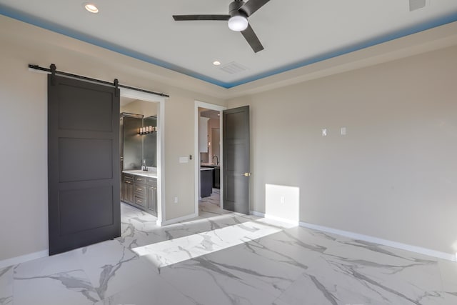 bedroom with ceiling fan, a barn door, a raised ceiling, and connected bathroom