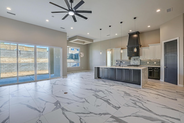 kitchen with pendant lighting, a center island with sink, ceiling fan, tasteful backsplash, and white cabinetry