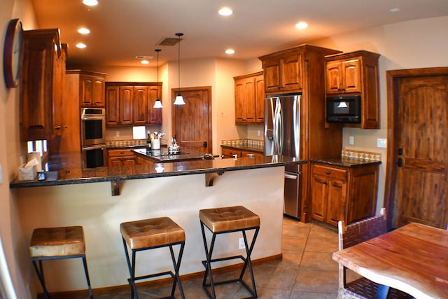 kitchen with black appliances, a kitchen breakfast bar, hanging light fixtures, tile patterned flooring, and kitchen peninsula