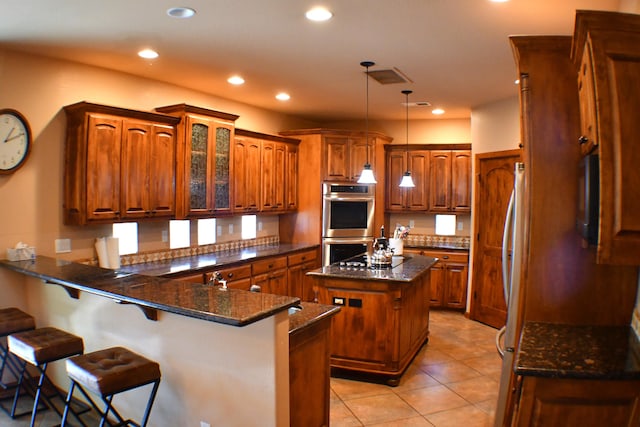 kitchen featuring hanging light fixtures, a kitchen breakfast bar, kitchen peninsula, dark stone counters, and a kitchen island