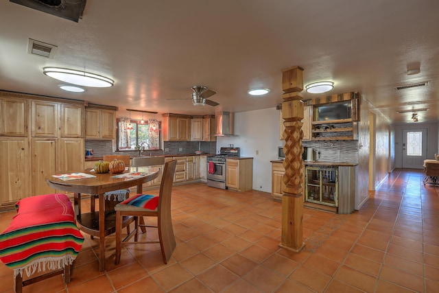 kitchen featuring tasteful backsplash, light tile patterned floors, wall chimney range hood, ceiling fan, and stainless steel range with gas cooktop