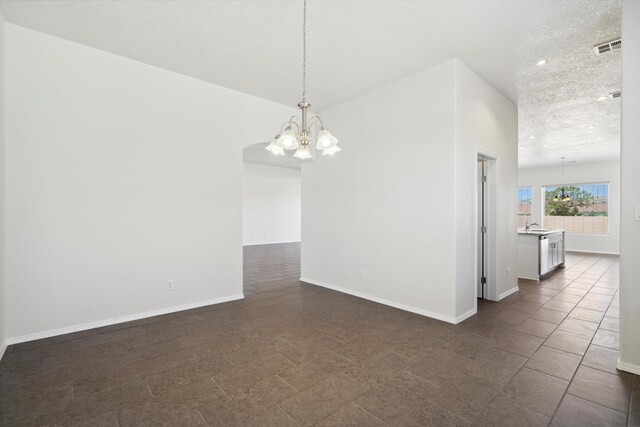 empty room featuring a textured ceiling, dark tile patterned flooring, and a notable chandelier