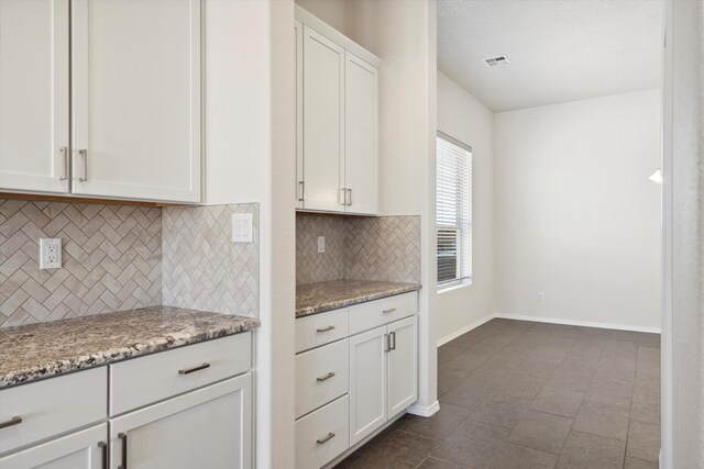 kitchen featuring backsplash, white cabinetry, and light stone counters