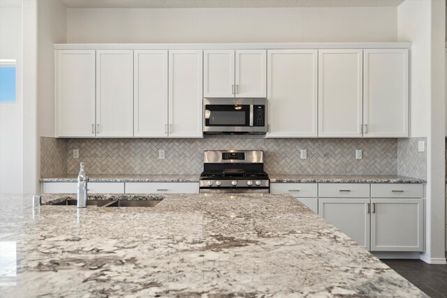 kitchen with backsplash, white cabinets, sink, light stone countertops, and stainless steel appliances