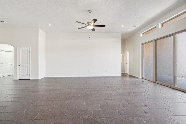 empty room featuring ceiling fan, dark tile patterned floors, a high ceiling, and a textured ceiling