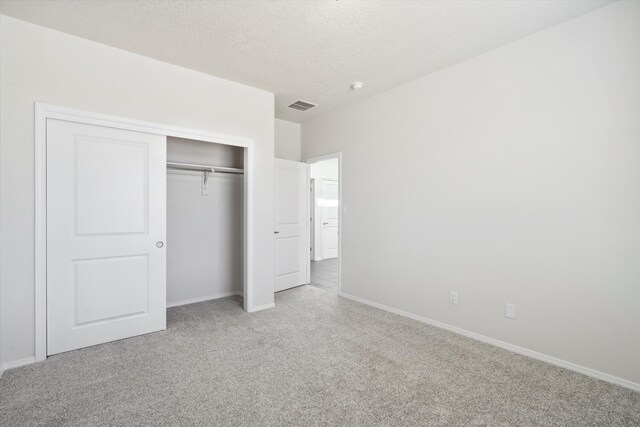 unfurnished bedroom with light colored carpet, a textured ceiling, and a closet