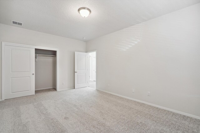 unfurnished bedroom featuring a textured ceiling, light carpet, and a closet