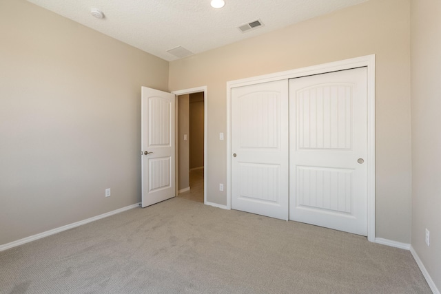 unfurnished bedroom with light carpet, a closet, and a textured ceiling