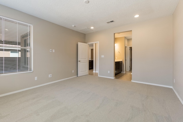 unfurnished bedroom with a textured ceiling, ensuite bathroom, and light colored carpet