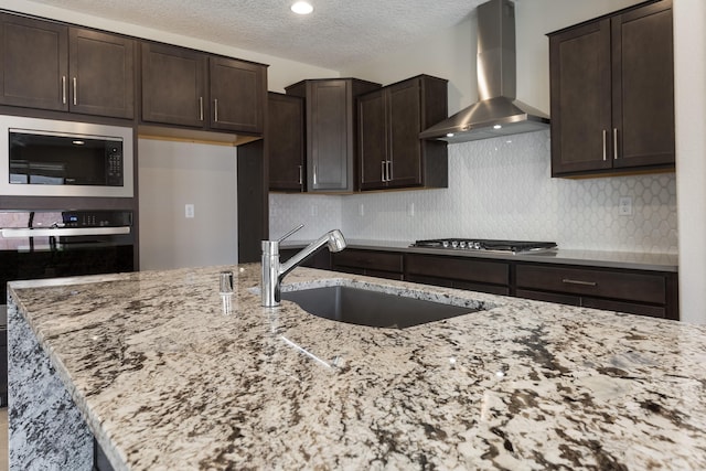 kitchen with light stone countertops, sink, black microwave, and wall chimney range hood