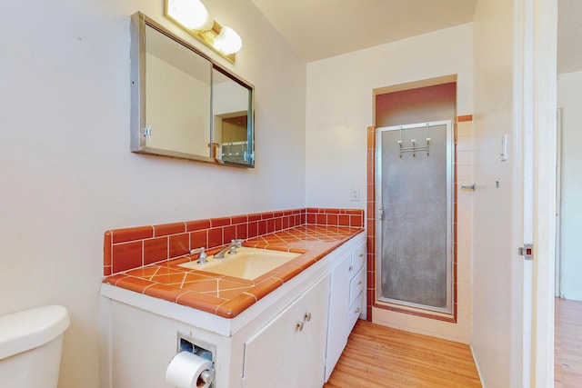 bathroom featuring a shower with shower door, vanity with extensive cabinet space, toilet, and hardwood / wood-style flooring