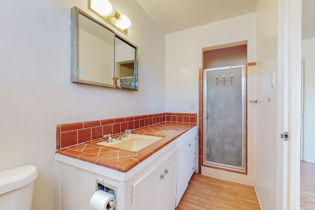 full bath featuring toilet, wood finished floors, vanity, backsplash, and a shower stall