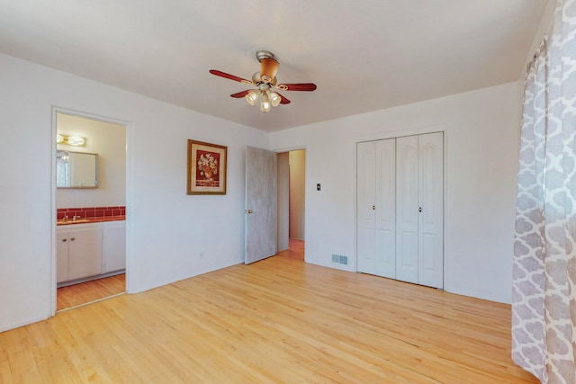 unfurnished bedroom featuring ceiling fan, a closet, ensuite bath, light wood-type flooring, and sink