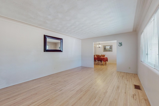 spare room featuring ornamental molding, light wood-type flooring, visible vents, and a notable chandelier