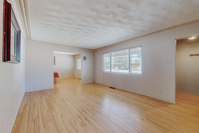 empty room with light wood-style floors, ornamental molding, and a textured ceiling