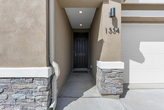 entrance to property with stone siding, stucco siding, and an attached garage