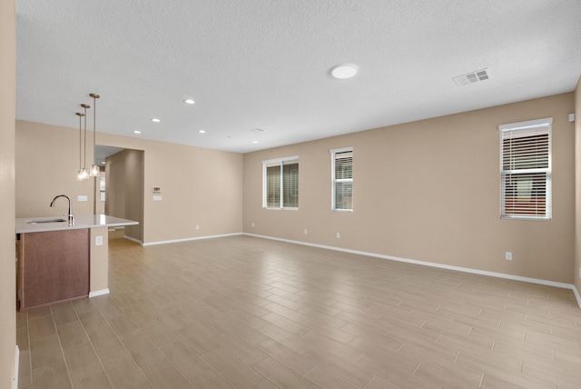 unfurnished living room with a sink, visible vents, baseboards, and a healthy amount of sunlight