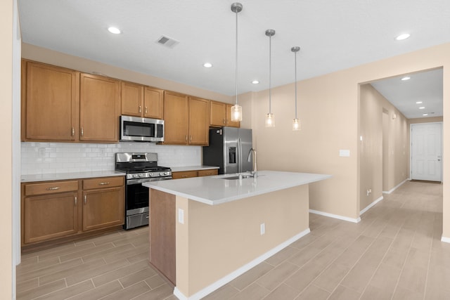 kitchen with visible vents, a kitchen island with sink, stainless steel appliances, light countertops, and decorative backsplash