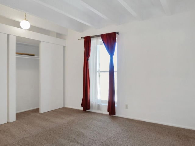 unfurnished bedroom with carpet, beam ceiling, and a closet