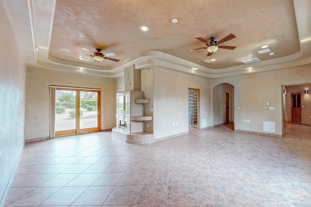 unfurnished living room featuring ceiling fan, a tray ceiling, and light tile patterned floors