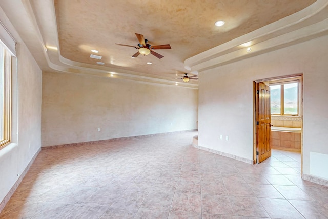 tiled empty room featuring ceiling fan and a raised ceiling