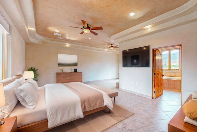 bedroom with a tray ceiling, light tile patterned floors, ceiling fan, and ensuite bathroom