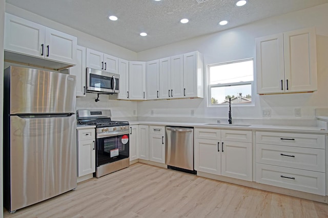 kitchen featuring sink, white cabinetry, light hardwood / wood-style flooring, a textured ceiling, and stainless steel appliances