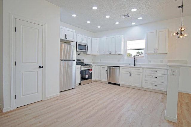 kitchen featuring appliances with stainless steel finishes, decorative light fixtures, white cabinetry, sink, and light hardwood / wood-style flooring