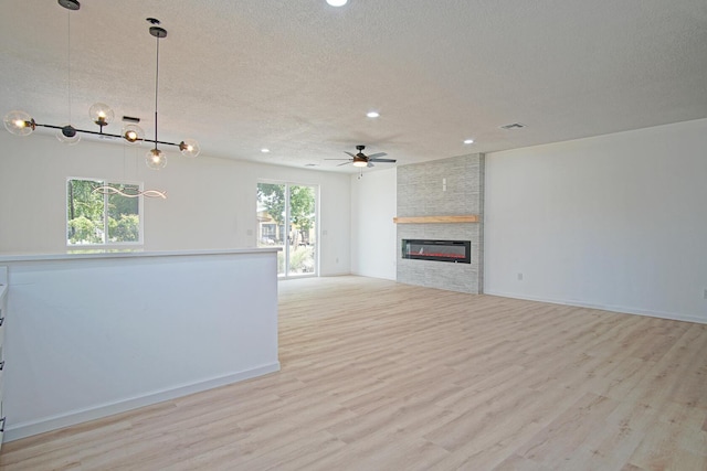 unfurnished living room featuring ceiling fan, a fireplace, a textured ceiling, and light wood-type flooring