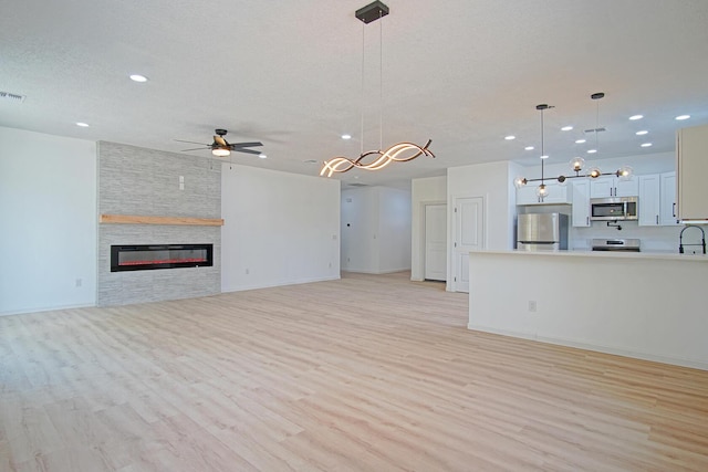 unfurnished living room featuring a stone fireplace, sink, ceiling fan, light hardwood / wood-style floors, and a textured ceiling