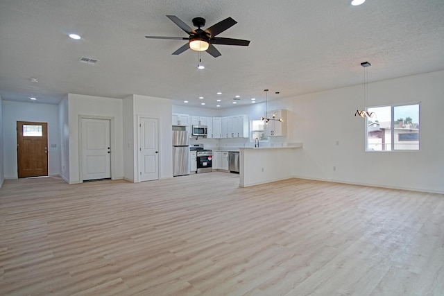 unfurnished living room with ceiling fan with notable chandelier, a textured ceiling, and light wood-type flooring