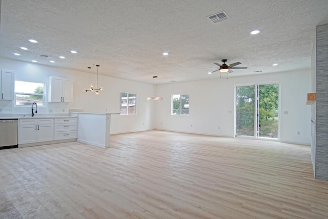 unfurnished living room featuring sink, ceiling fan with notable chandelier, light hardwood / wood-style flooring, and a textured ceiling